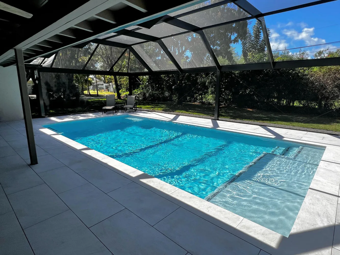 Modern rectangular inground pool with full screen enclosure in Palmetto Bay by Bluewater Design Studio